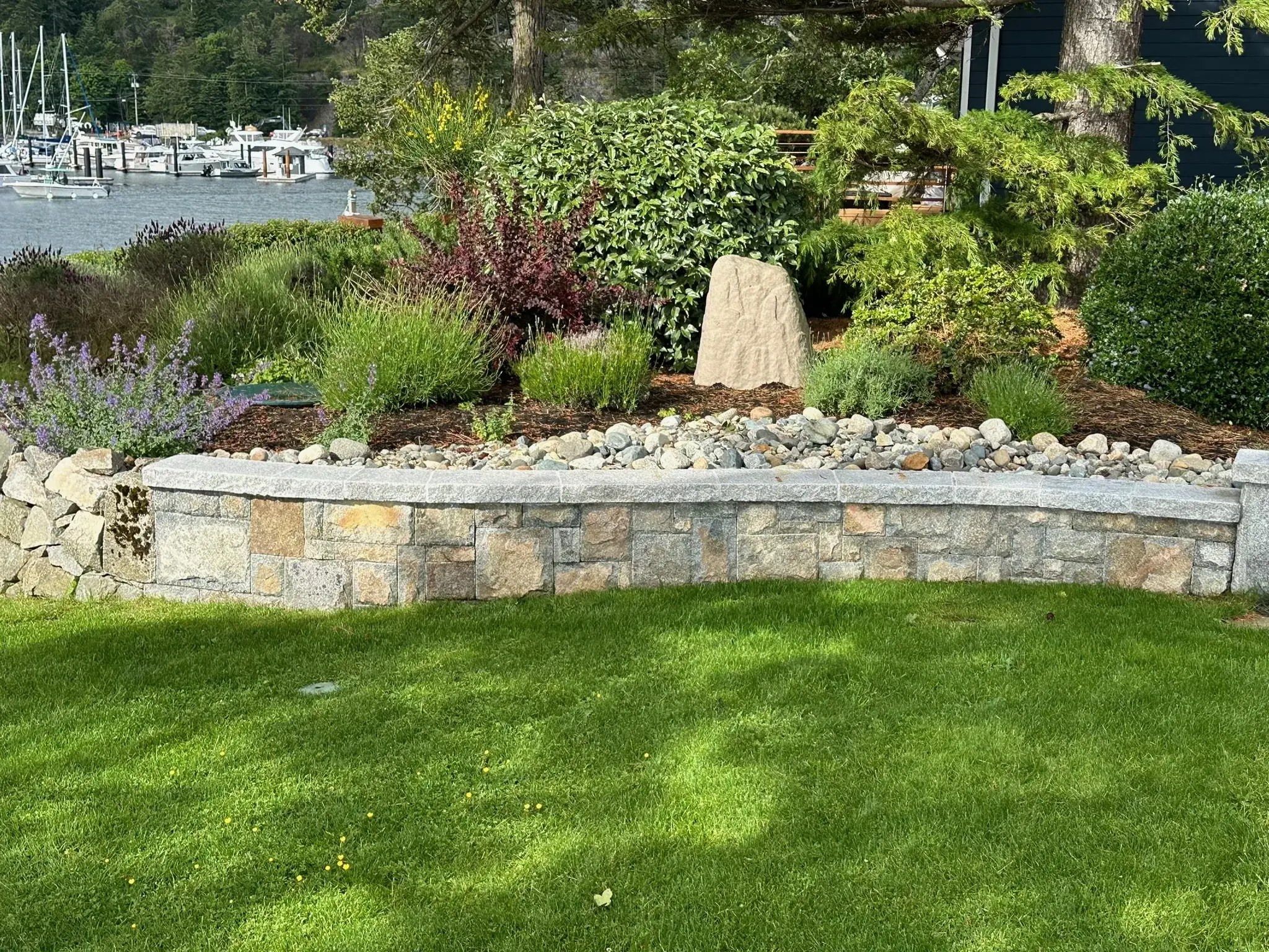 Stone garden wall and planted beds above a lawn, looking out to the marina
