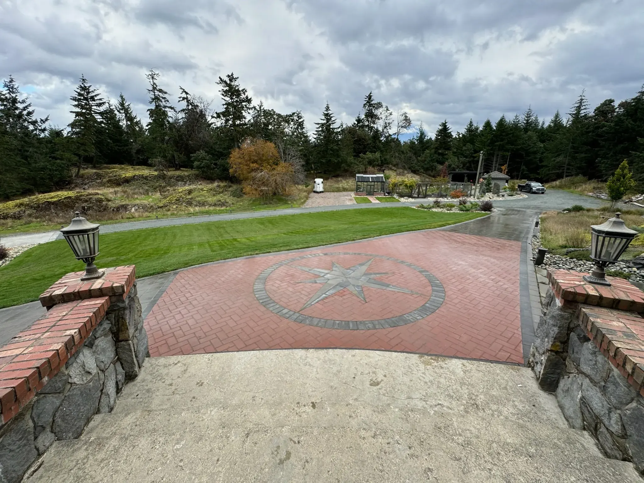 Brick driveway apron with a stone compass inlay and a lamp post on each side
