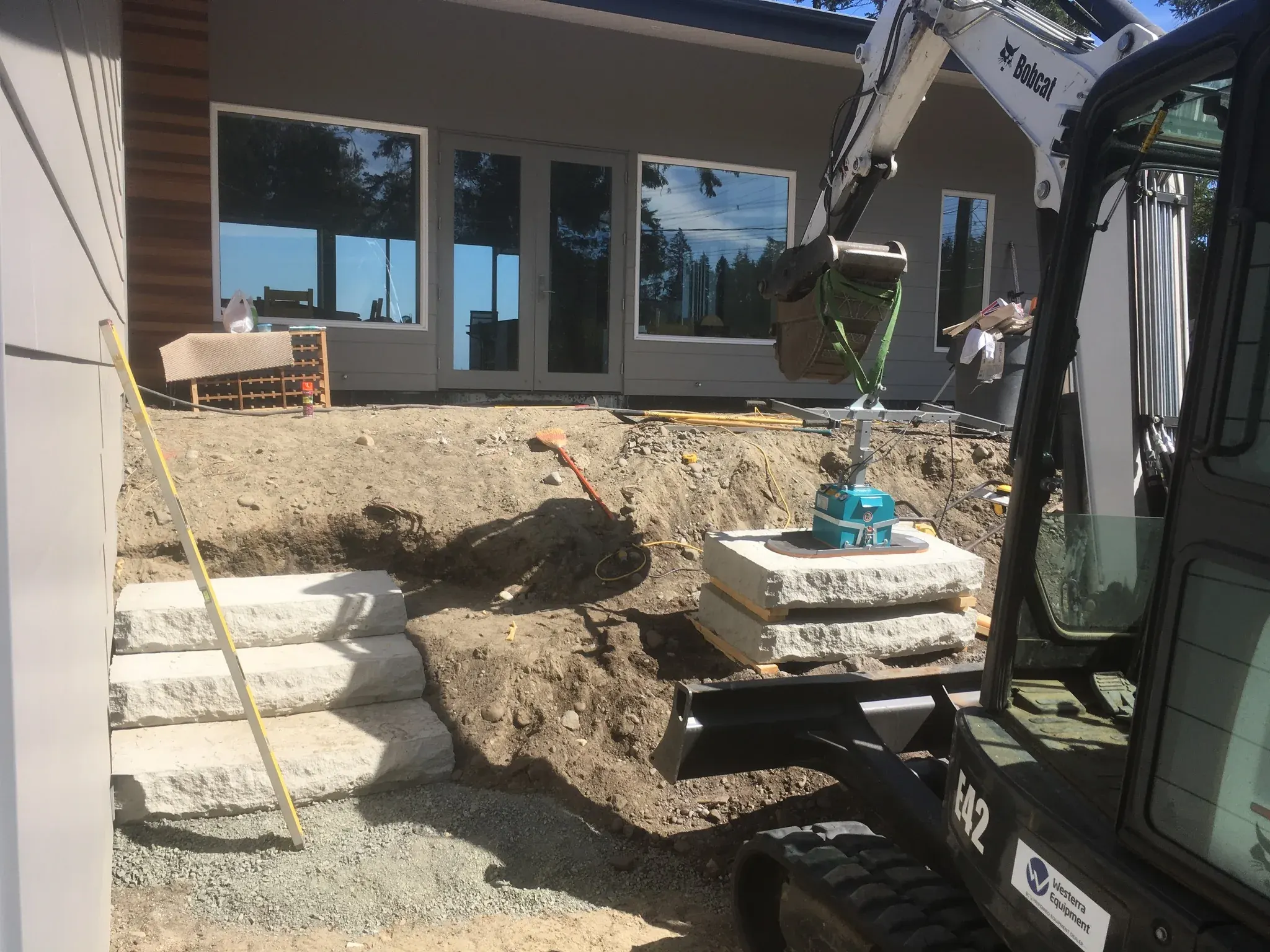 Excavator setting stone steps beside a house foundation