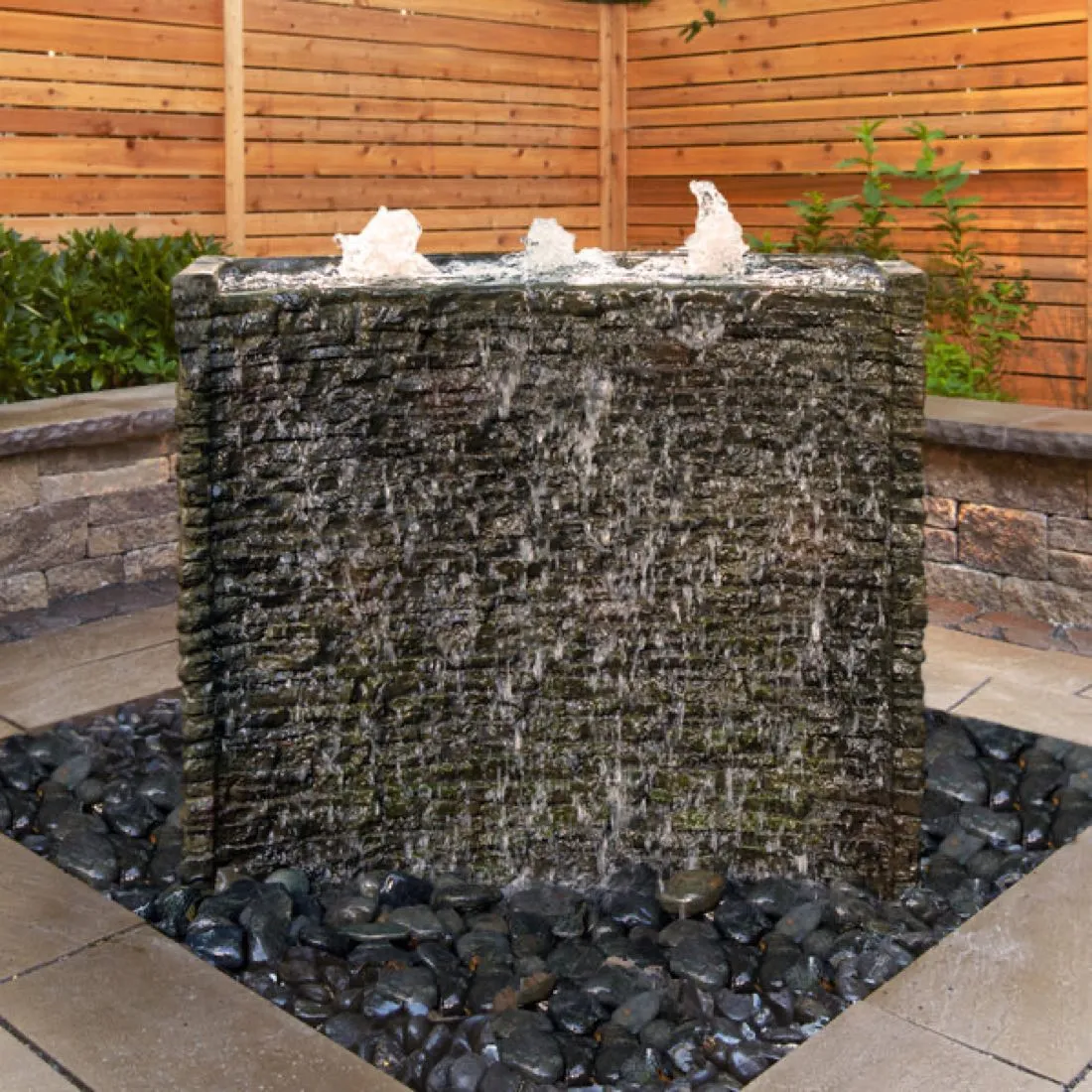 Stacked-slate spillway wall fountain running into a pebble basin on a paved patio
