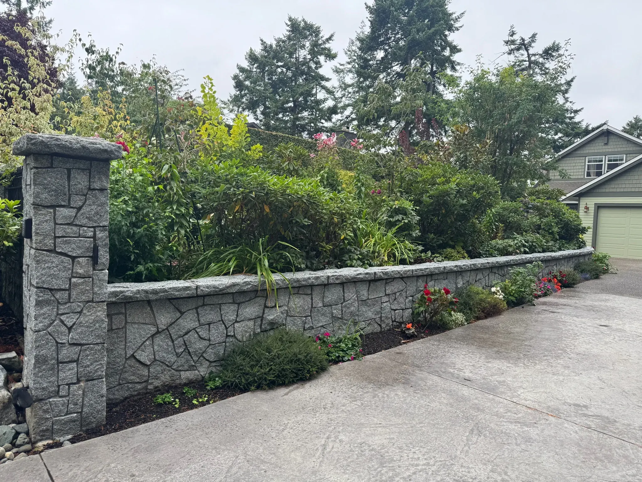 Stone pillar and wall running along a driveway with planted borders