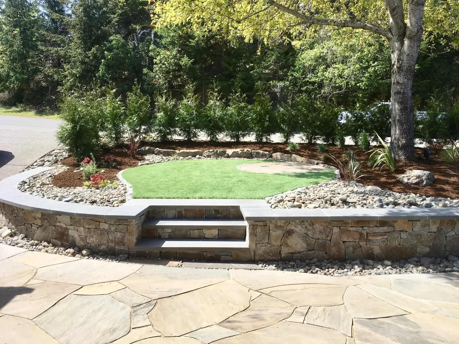 Dry-stone retaining wall wrapping a level lawn and flagstone terrace on a Mid-Island property